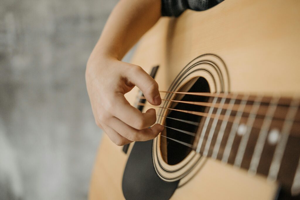 Detailed view of a hand strumming an acoustic guitar, showcasing the strings and soundhole.